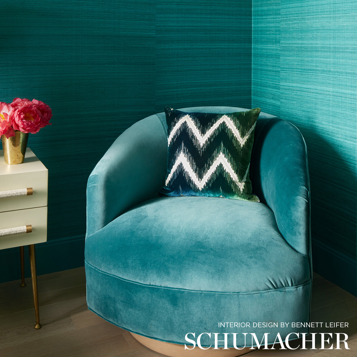 Teal velvet round armchair with curved arms and a chevron cushion in a turquoise-walled room.