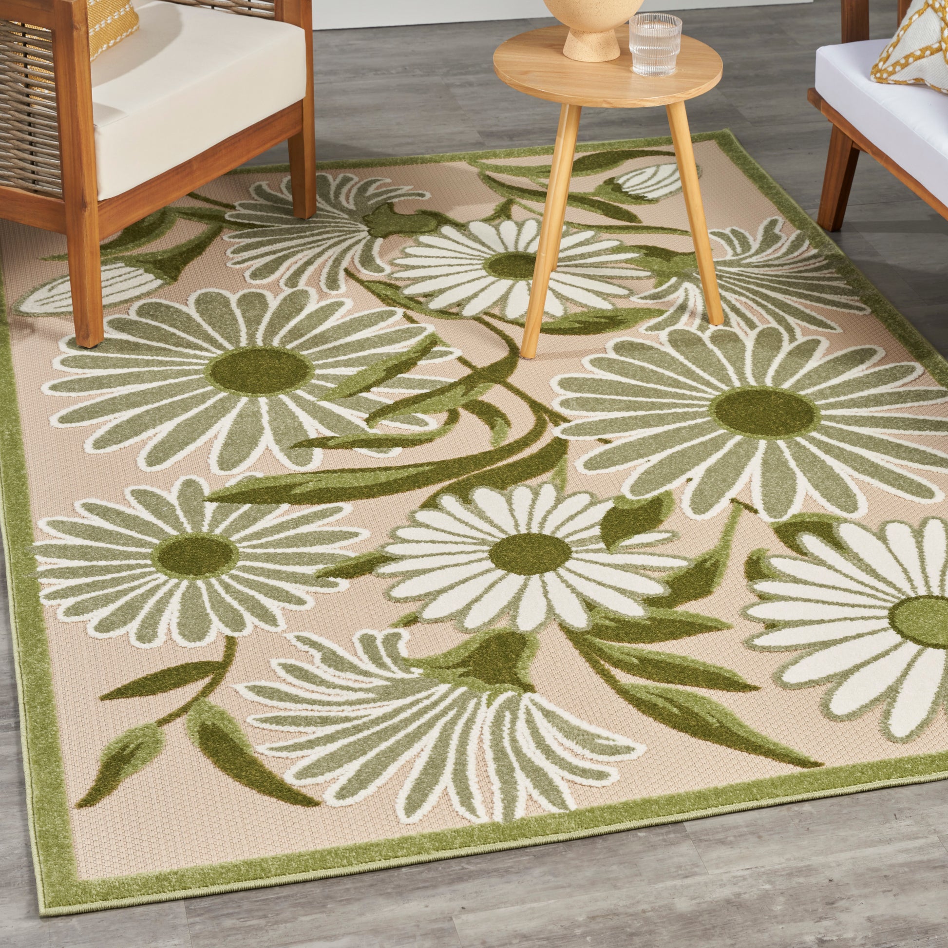 Beige outdoor rug with large white daisies and green stems, olive border; patio area with wooden chairs.