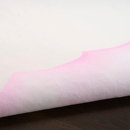 Soft pink gradient fabric with curled edge resting on a dark wood tabletop.