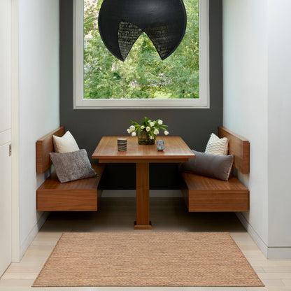 Cozy wooden dining nook with built-in benches, square table, cushions, black pendant lamp, window greenery, beige rug.