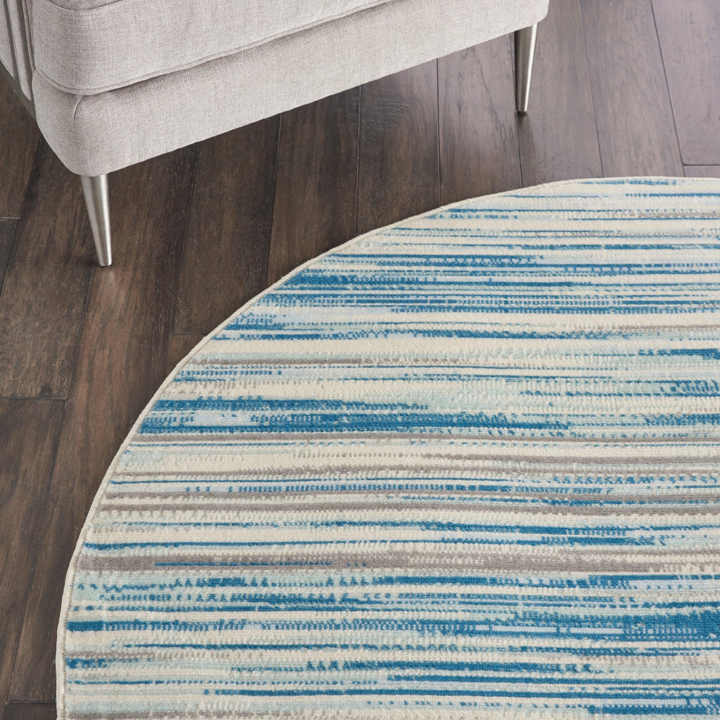 Round rug with blue striped pattern on white, on dark wood floor beside a light gray sofa with metal legs.