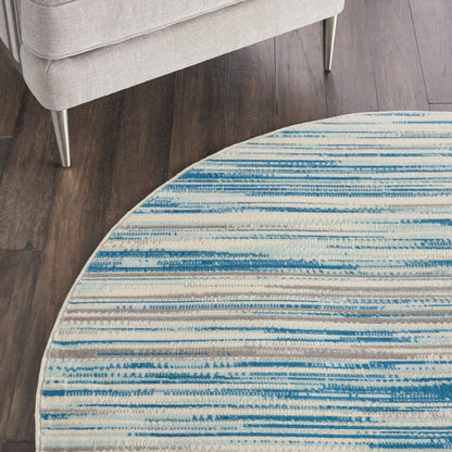 Round rug with blue striped pattern on white, on dark wood floor beside a light gray sofa with metal legs.