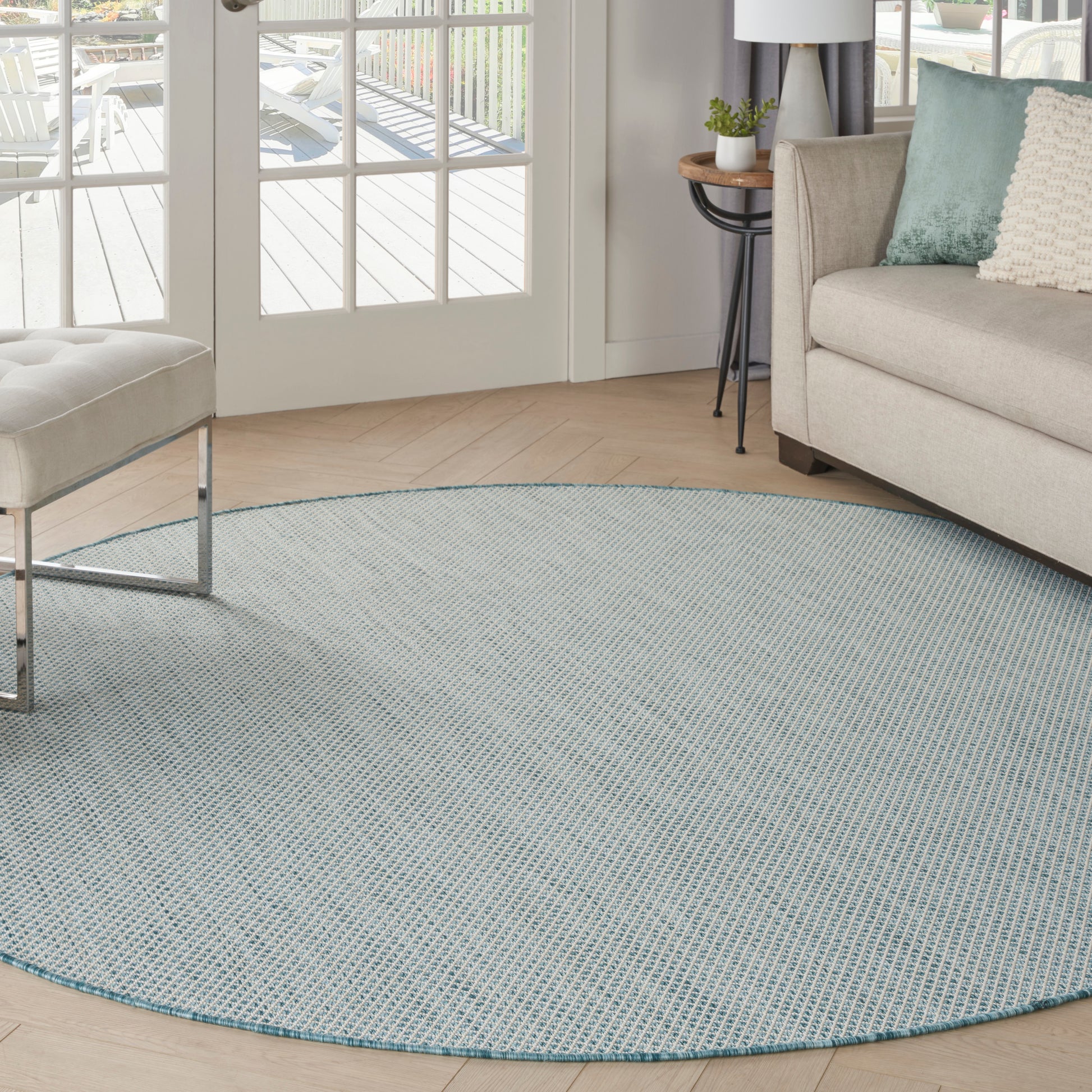 Light-blue woven round area rug in a bright living room with a beige sofa and glass doors.