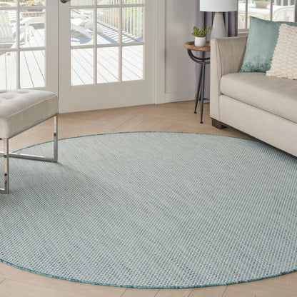 Light-blue woven round area rug in a bright living room with a beige sofa and glass doors.