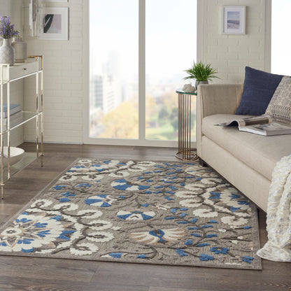 Neutral living room with a blue floral patterned area rug, beige sofa, throw blanket, and a green plant by a large window.