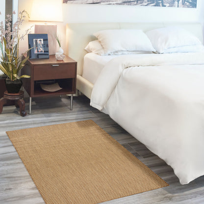 White bed with plush duvet and pillows, dark wood nightstand, lamp, plant, and beige woven rug on gray wood floor.