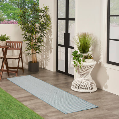 Blue textured rug runner on wood floor in bright entryway with potted plants and black-framed glass doors.