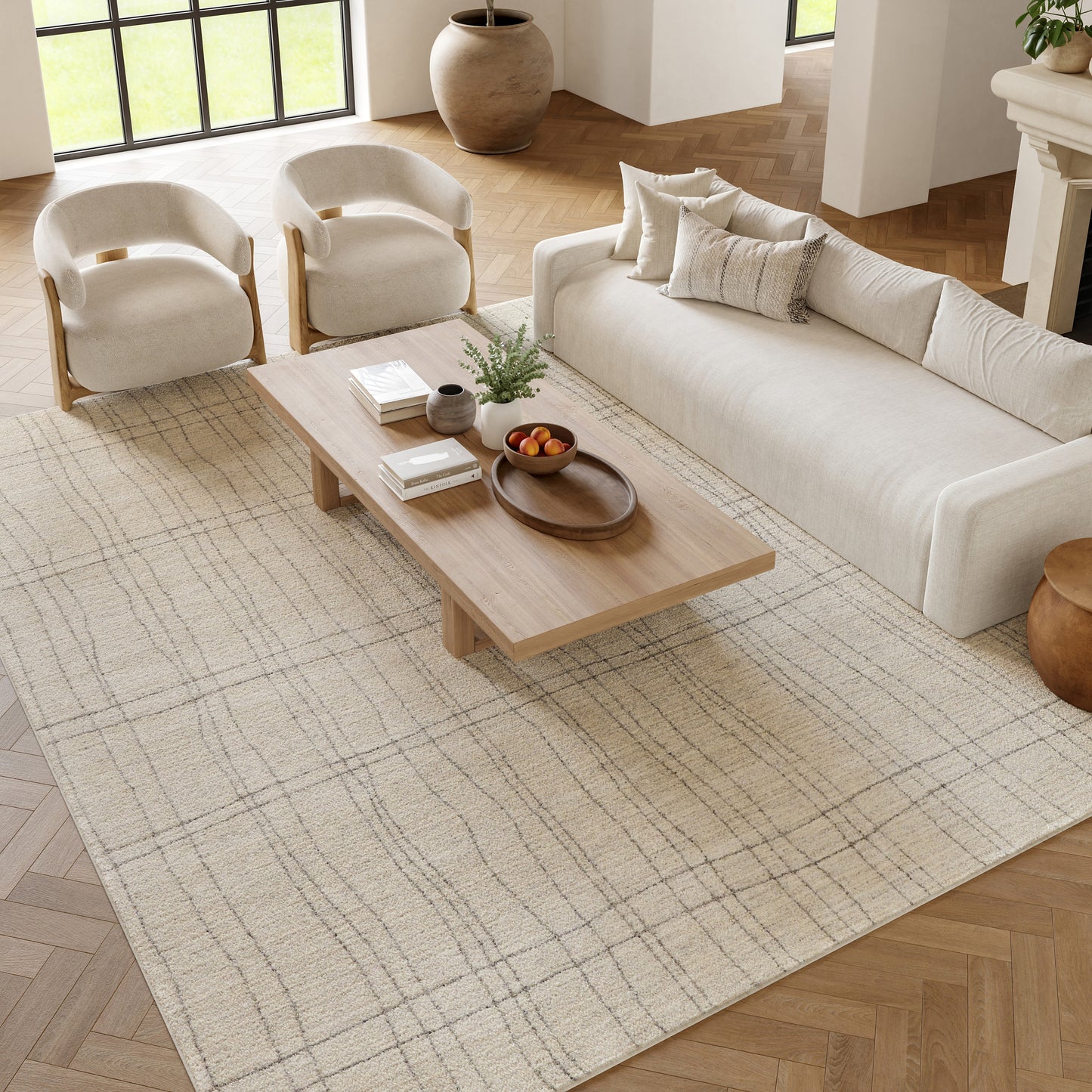 Neutral living room with cream sofa & rounded armchairs, wooden coffee table on a beige textured rug, warm natural light.