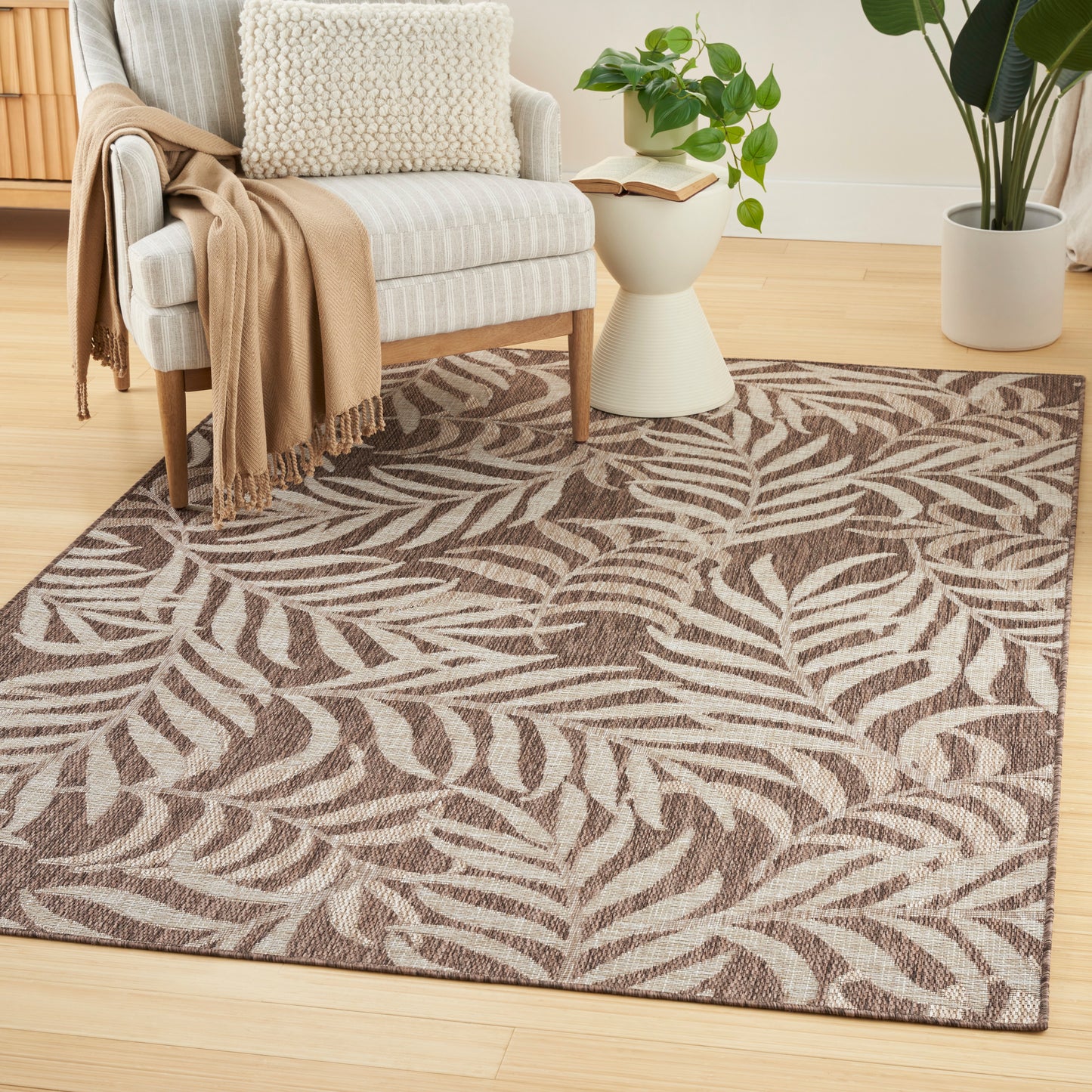 Leaf-pattern rug in brown and beige on wood floor under a light striped armchair with a tan throw and cream pillow.