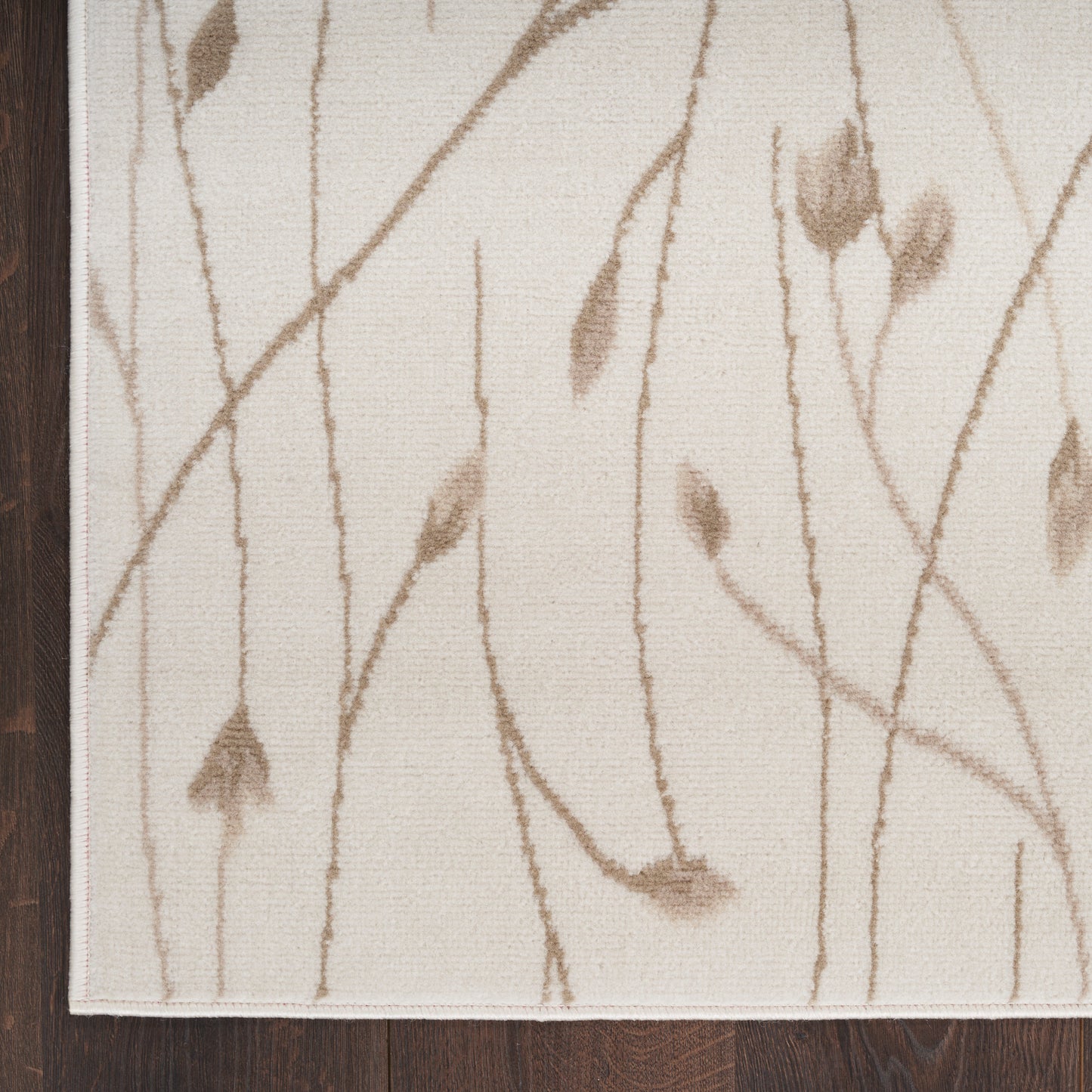 Beige area rug with brown twig and leaf motif on cream background; dark wood floor edge visible.