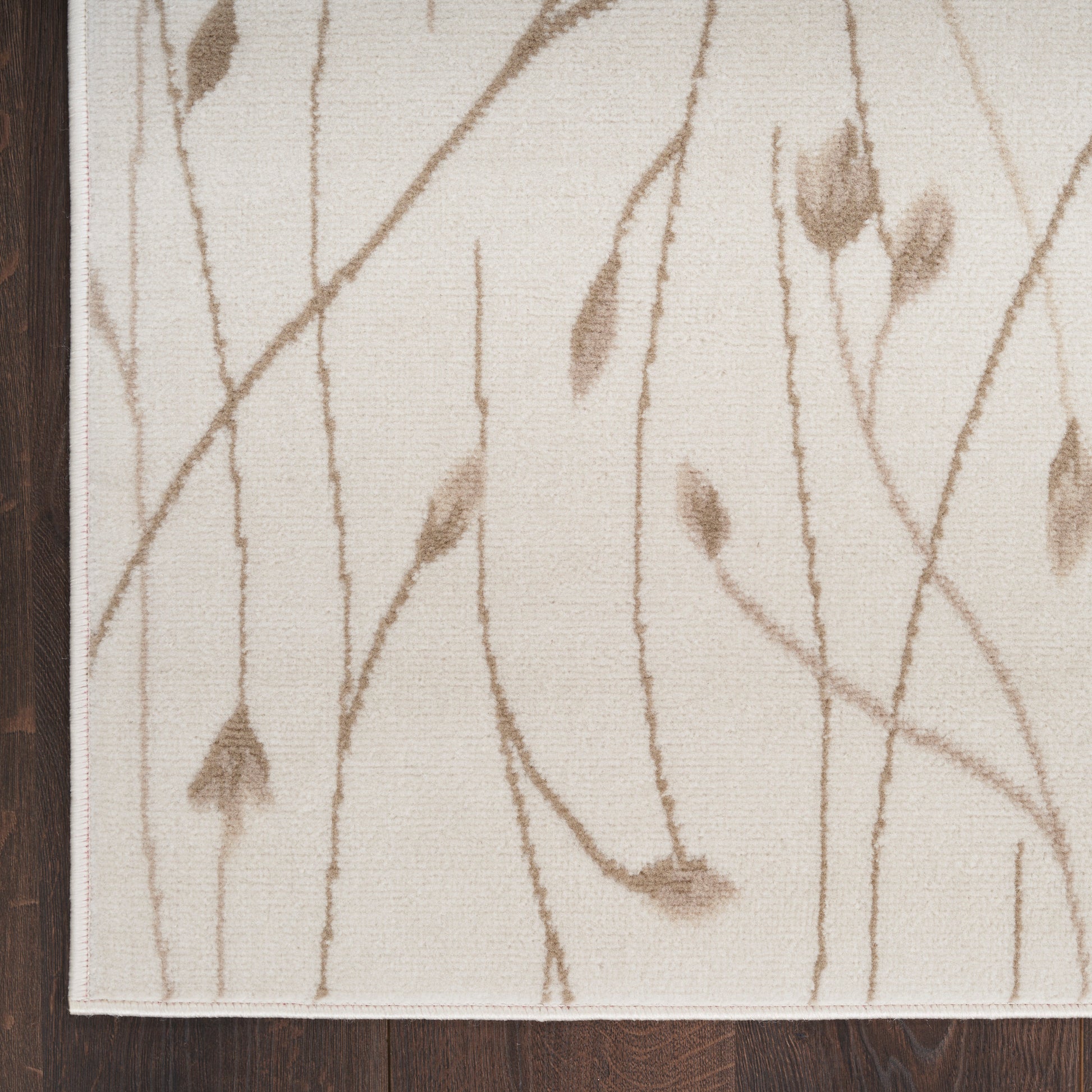 Beige area rug with brown twig and leaf motif on cream background; dark wood floor edge visible.