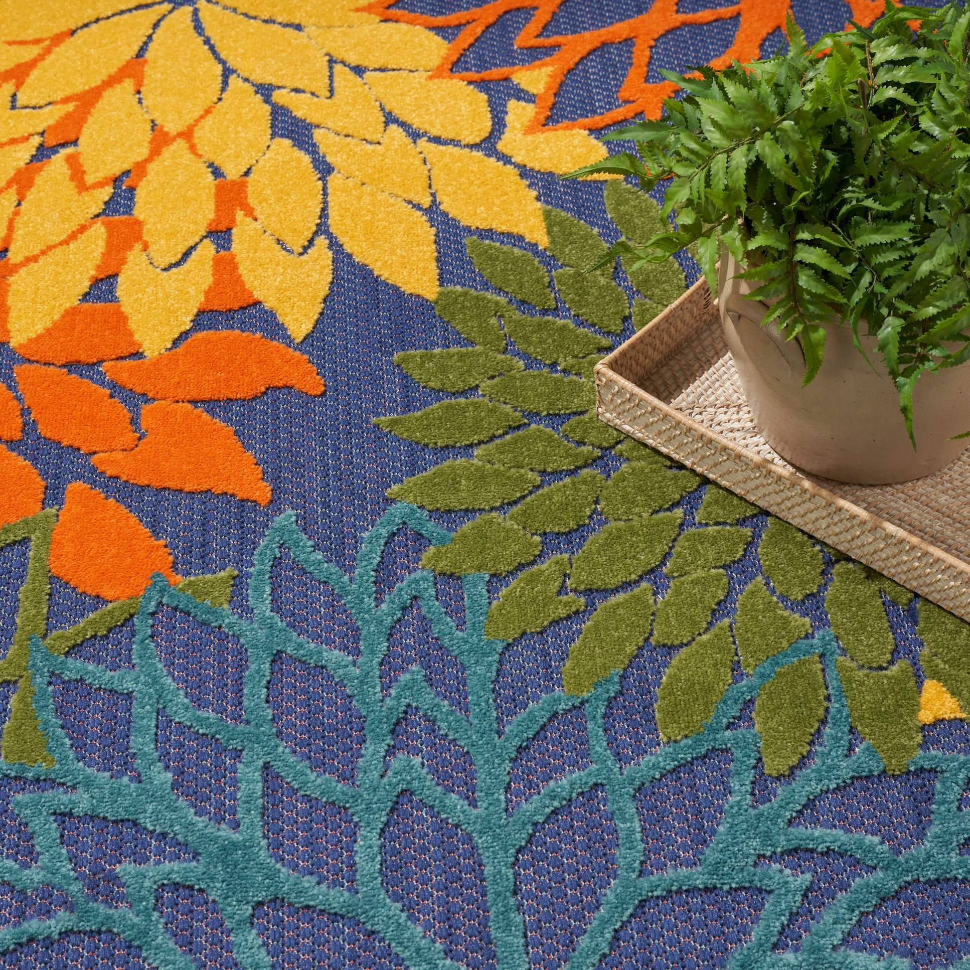 Round outdoor rug with a vibrant leaf pattern in orange, yellow, teal and green on blue.