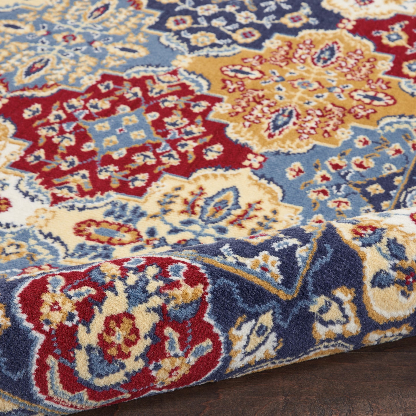 Colorful Persian-style rug with red, blue, cream and gold floral motifs; ornate woven pattern on wood floor.