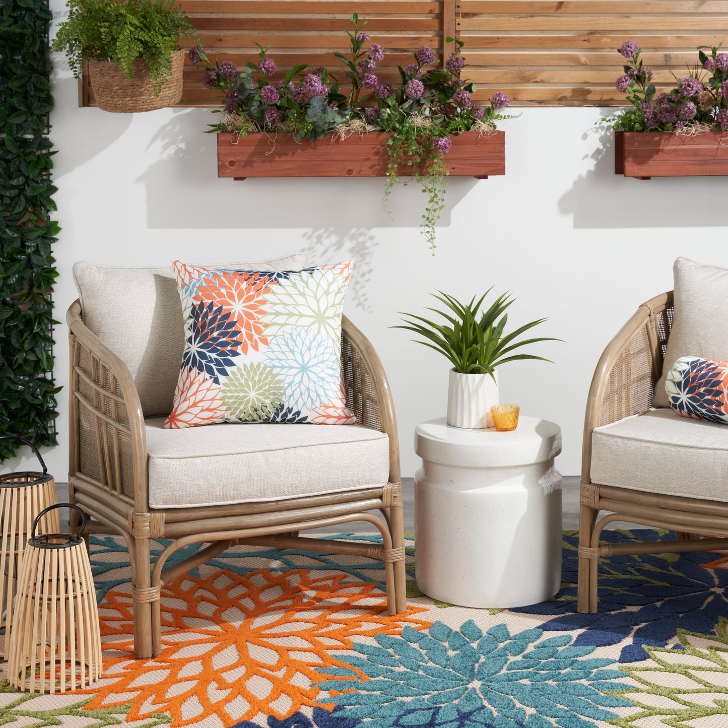 20" x 20" outdoor rug in tropical multicolor pattern with teal and orange accents, shown with beige-cushioned wicker lounge chairs and a white side table.