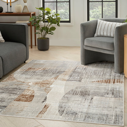 Geometric abstract area rug in beige, gray and taupe on light wood floor beside a gray sofa and armchair.