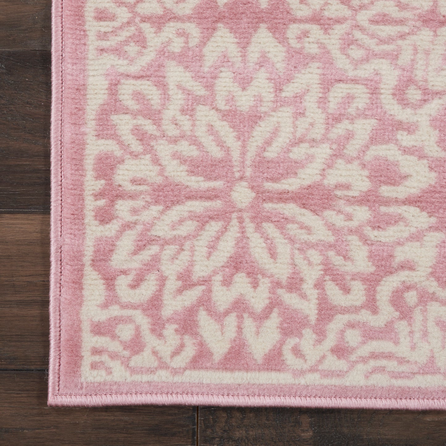 Soft pink rectangular rug with a white damask pattern and pink edge trim.