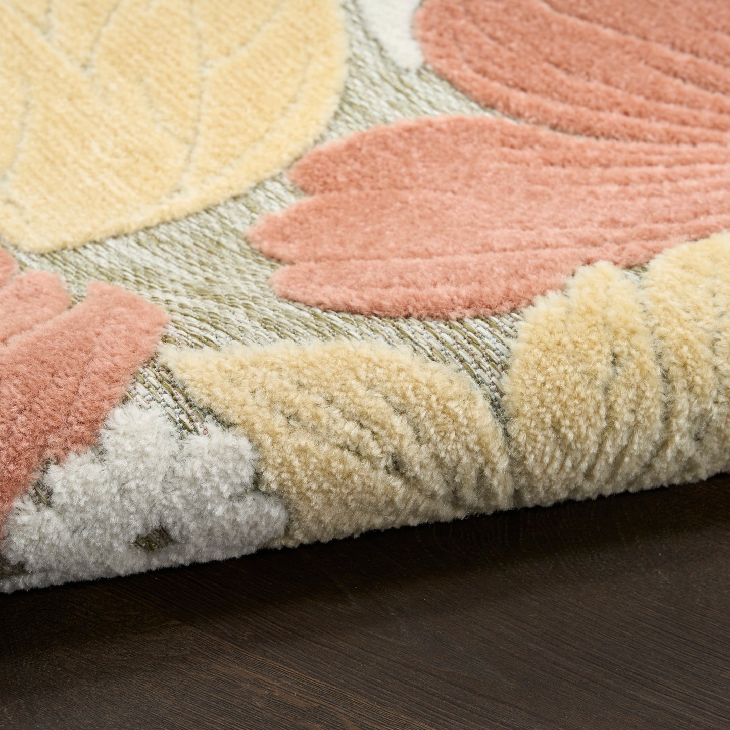 Pastel leaf-pattern shag rug in peach, yellow, and beige tones with a rolled edge on dark wood floor.