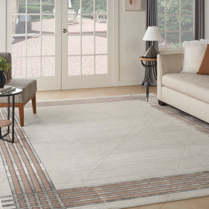 Light gray geometric area rug with brown striped border in a bright living room featuring a beige sofa & glass doors.
