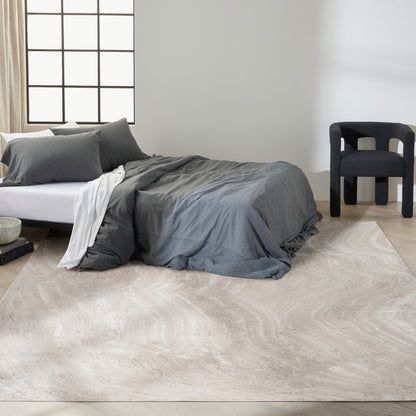 Grey and beige patterned area rug on the floor near a low-profile bed; visible are grey bedding with white sheets, charcoal pillows, and a black chair by a window.