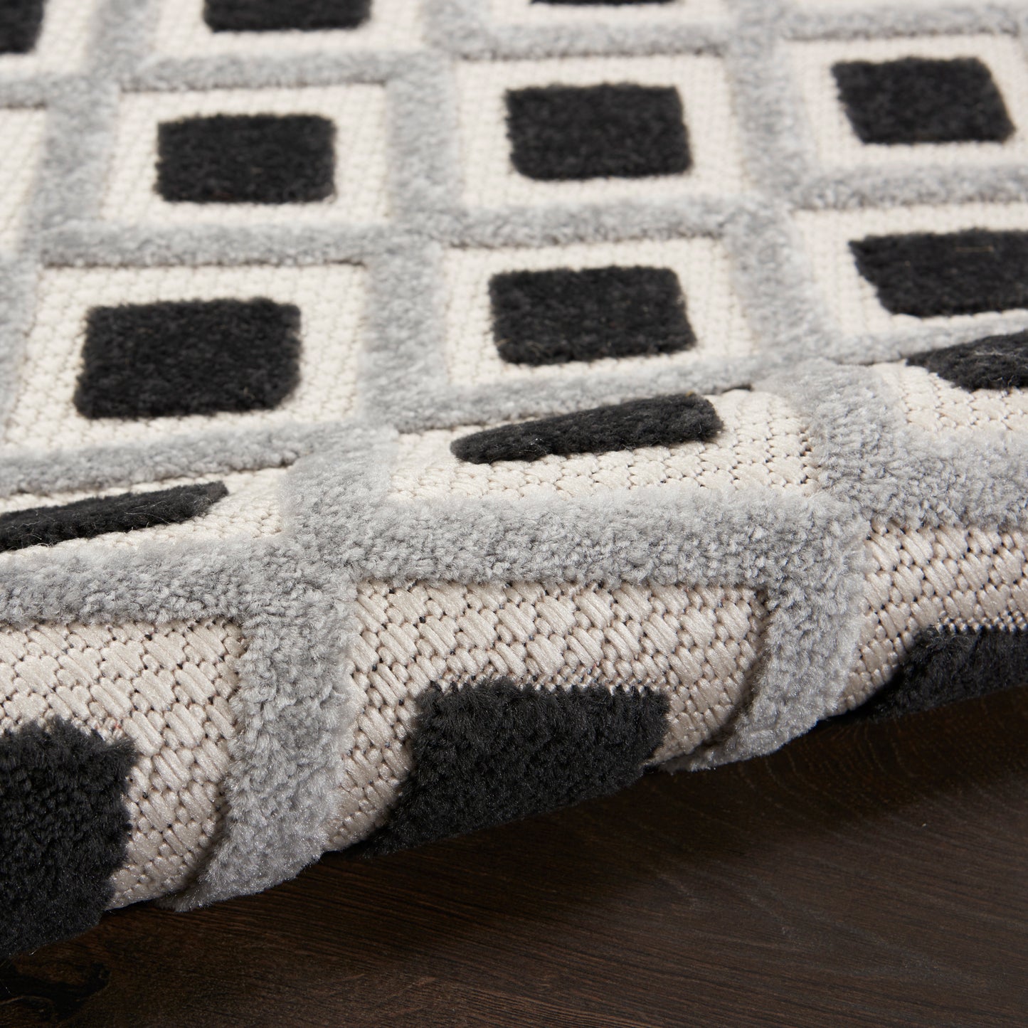 Soft plush area rug with a gray square-grid pattern and black centers on a dark wood floor.