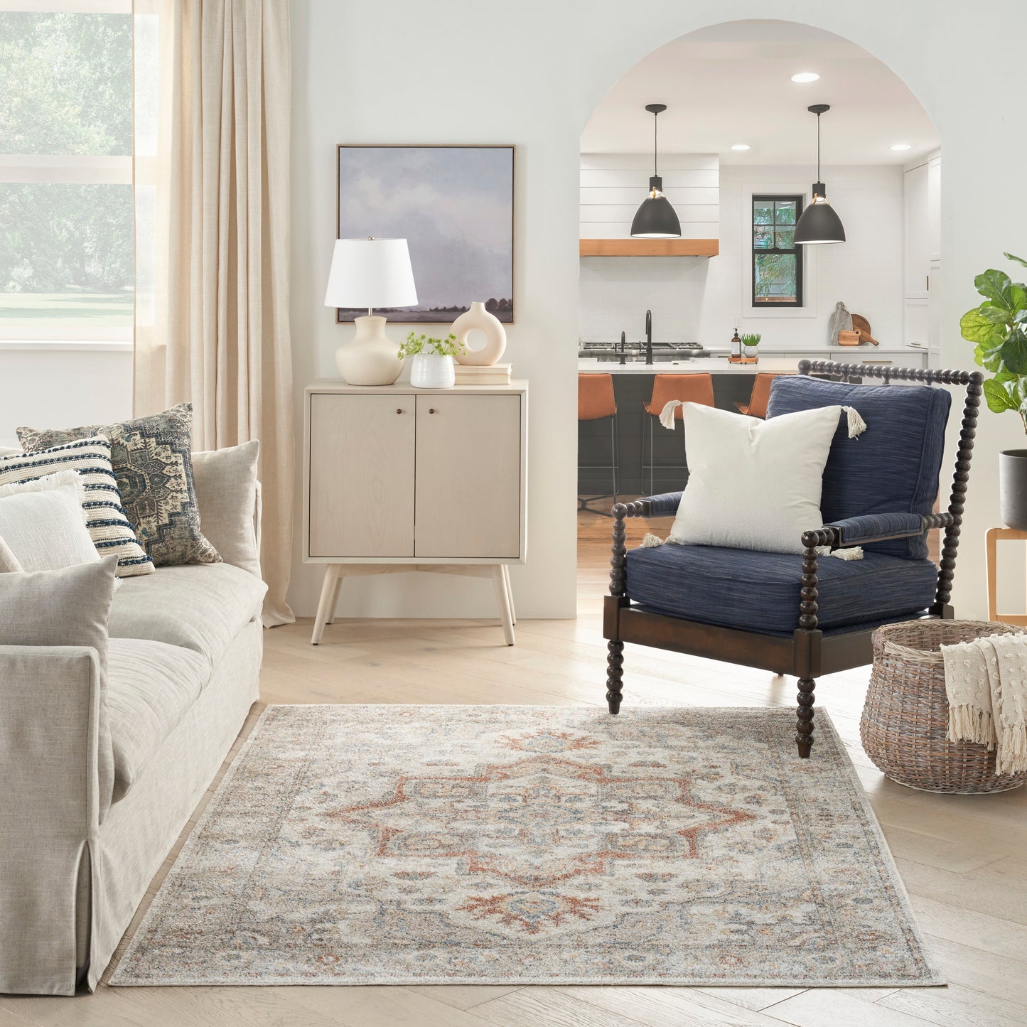 Neutral living room with beige sofa, navy armchair, light wood cabinet, woven basket, and blue-orange patterned area rug.
