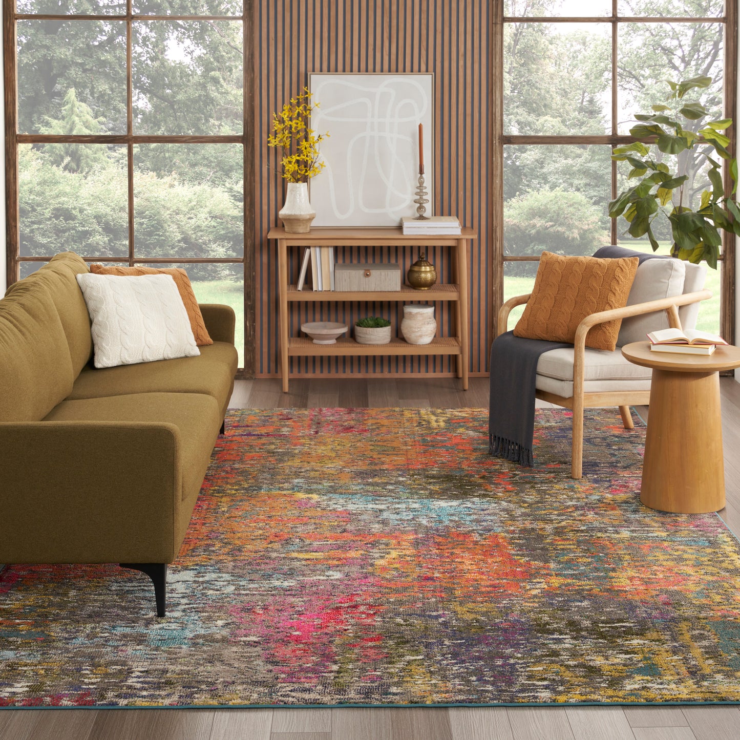 Olive-green sofa and light wood armchair with orange pillow, multicolor abstract rug, wooden slat wall, console with art