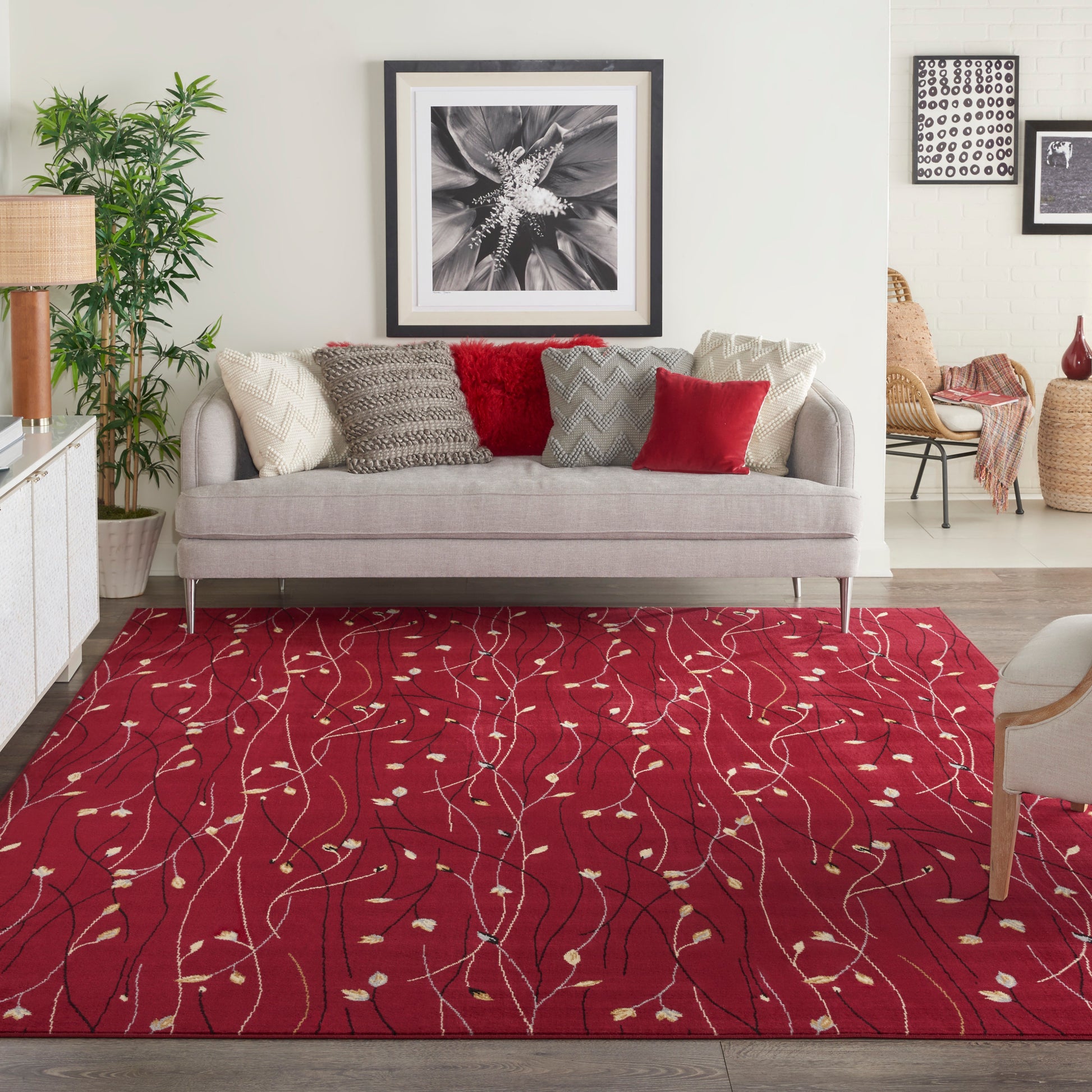 Living room with a red patterned area rug featuring white leaf-like vines, beige sofa with textured pillows, and framed art.