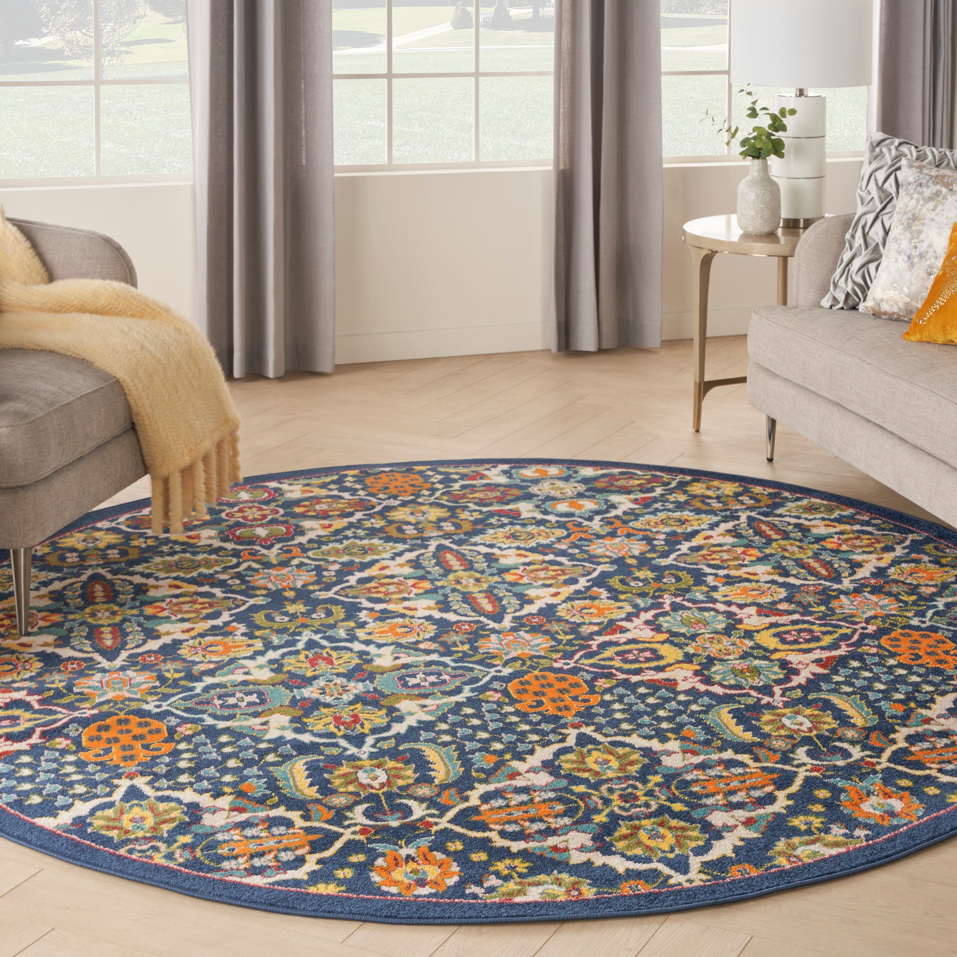 Round floral area rug with navy background and multicolor blossoms in orange, teal, yellow; living room with gray sofas.