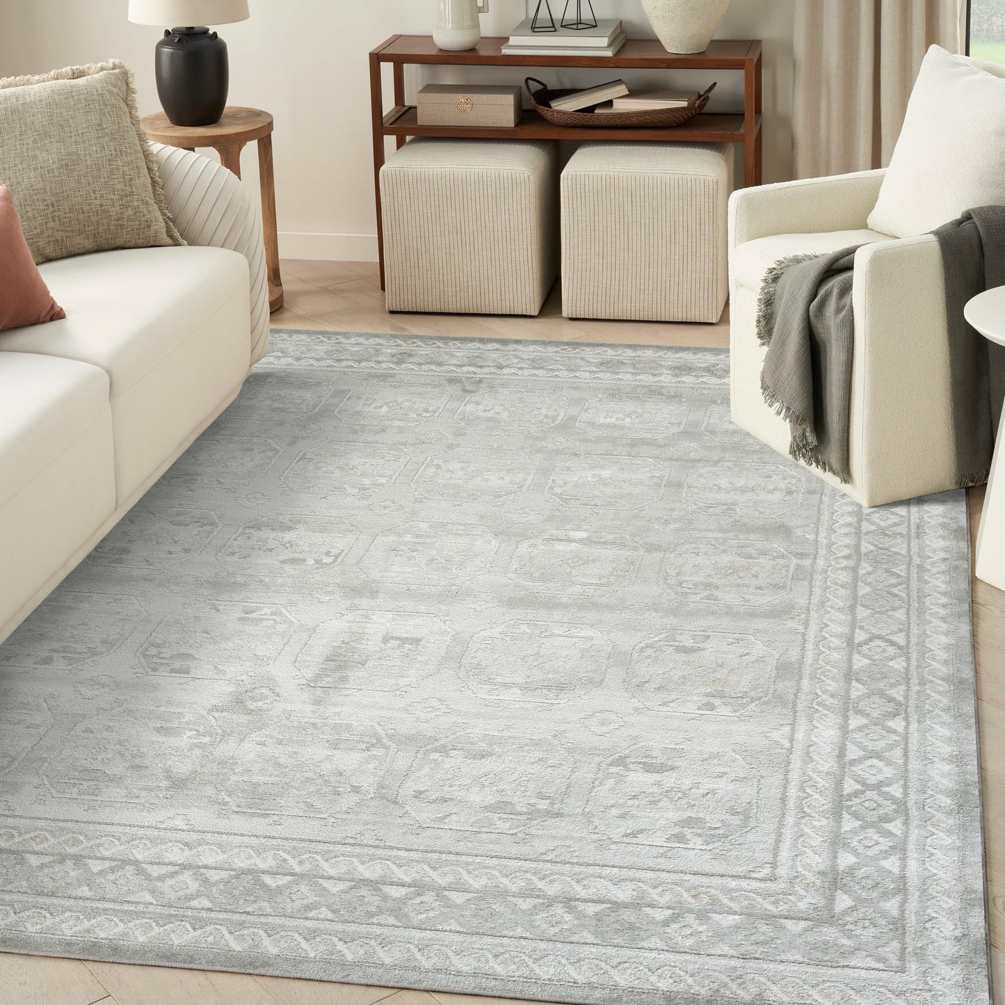 Soft gray-blue patterned area rug with geometric border in a neutral living room with cream sofa.