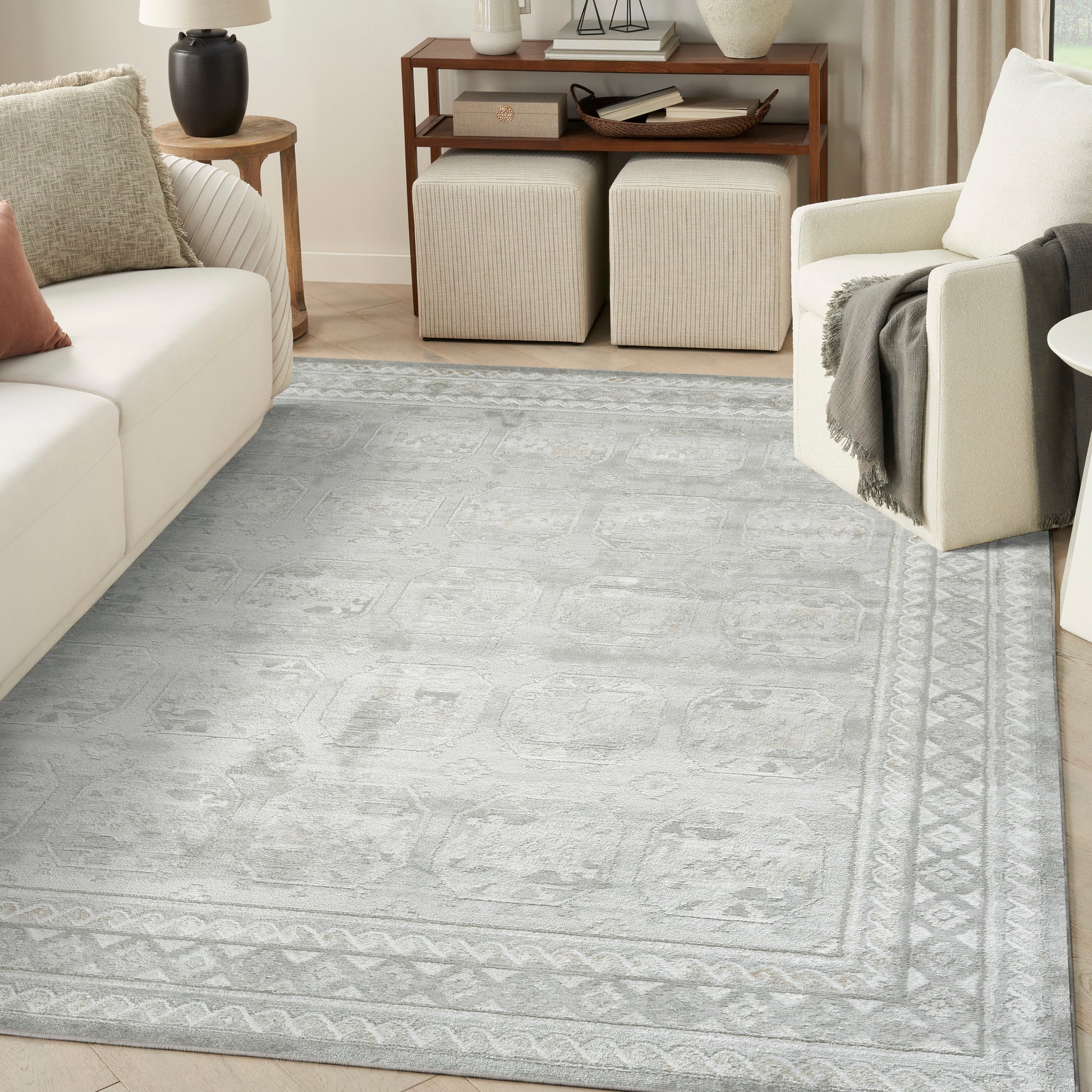 Soft gray-blue patterned area rug with geometric border in a neutral living room with cream sofa.