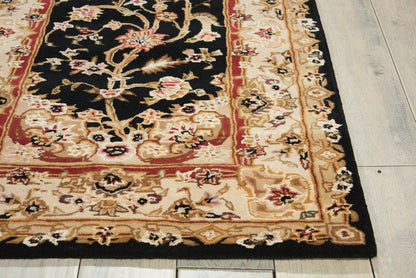 Persian-style rug with black central field, cream-gold & red floral border on light wood floor.