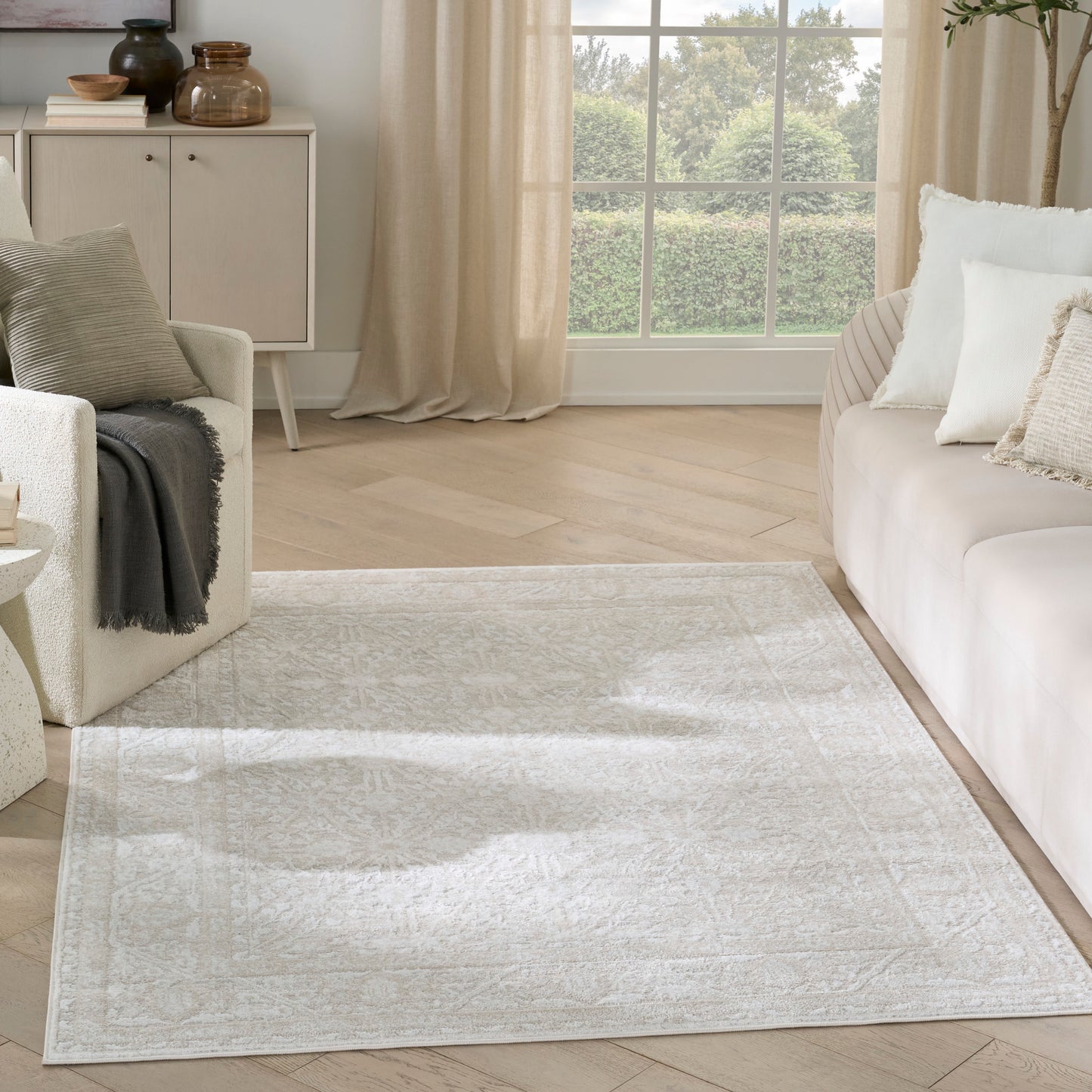 Soft cream living room with beige sofa, textured rug, light wood floors, and a large window with beige curtains.
