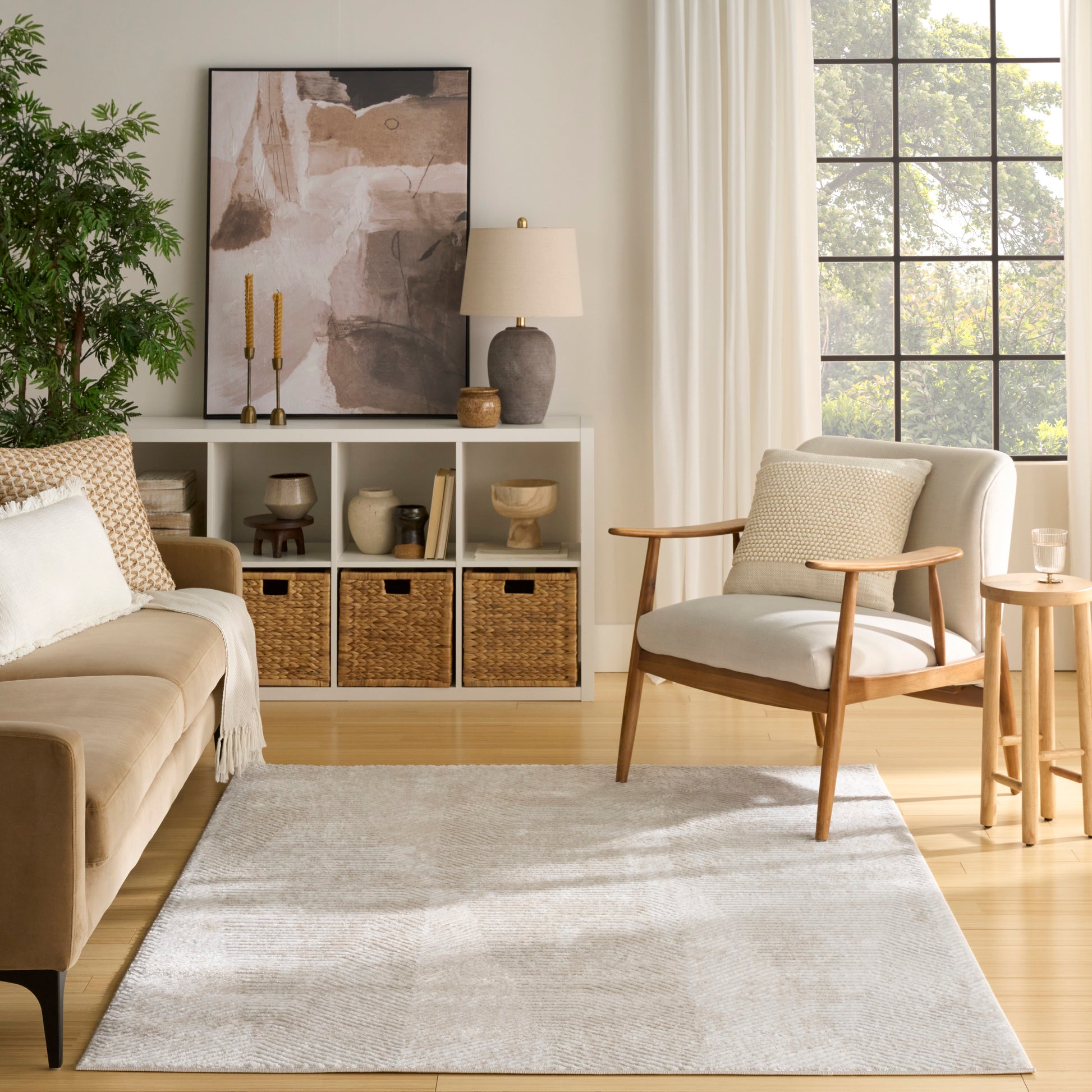 Neutral Scandinavian living room with beige sofa, light wood chair, gray rug, woven baskets, abstract art, and grid window.