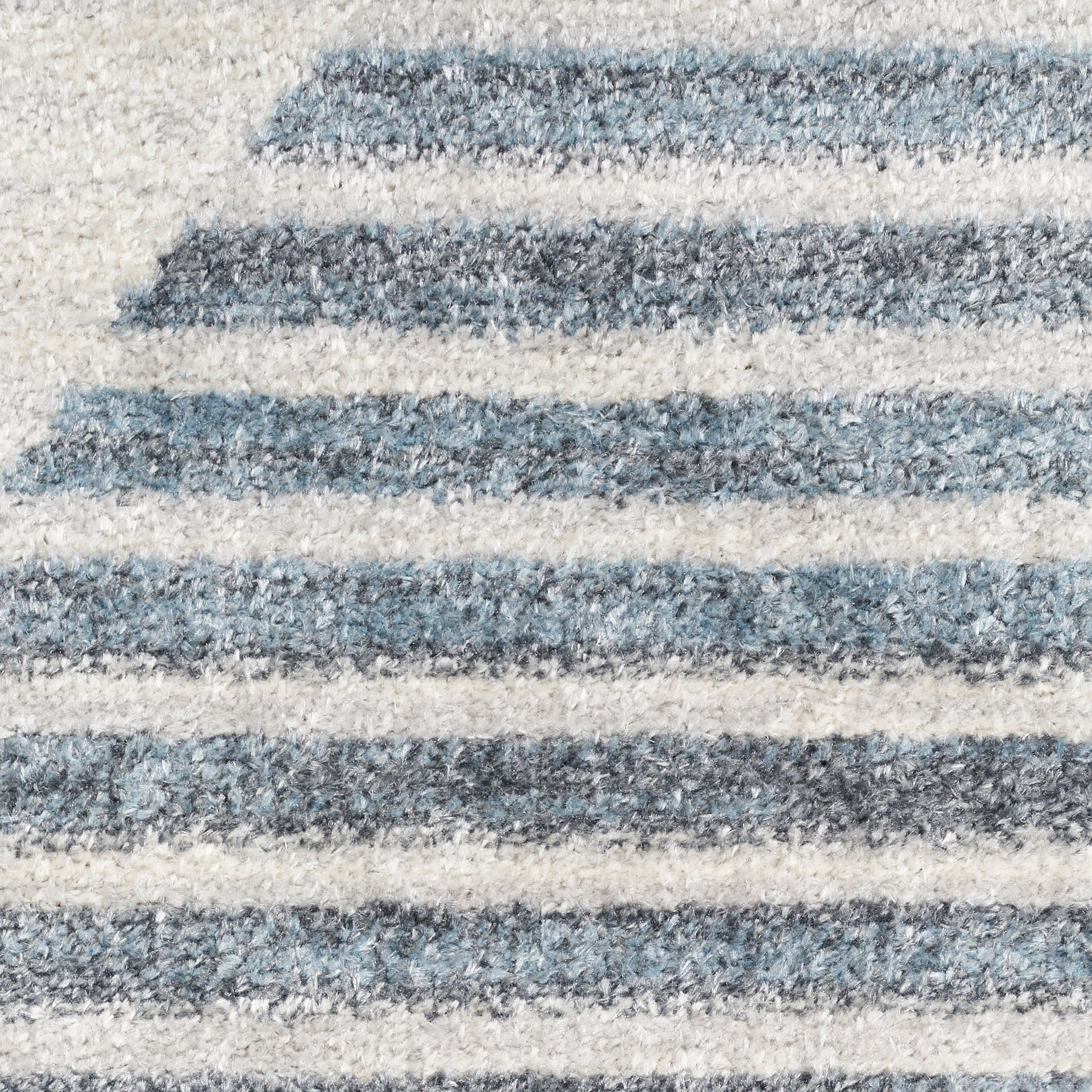 Close-up of a blue and cream striped rug with soft pile and alternating thick and thin horizontal stripes.