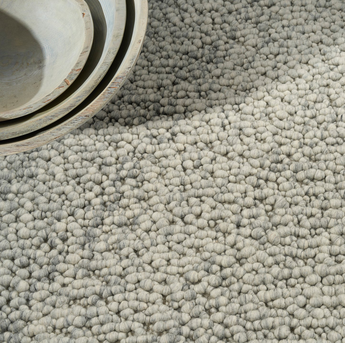 Close-up of a light gray boucle rug with thick loop pile, soft woven texture and a rolled edge.