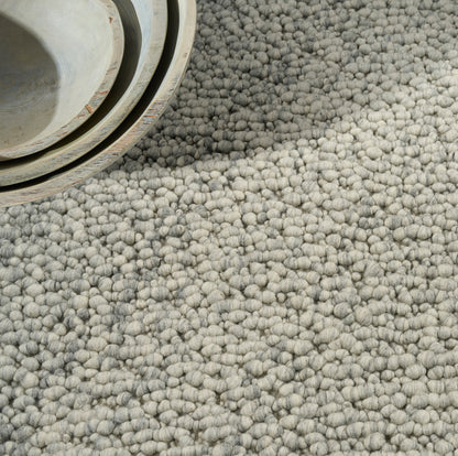 Close-up of a light gray boucle rug with thick loop pile, soft woven texture and a rolled edge.
