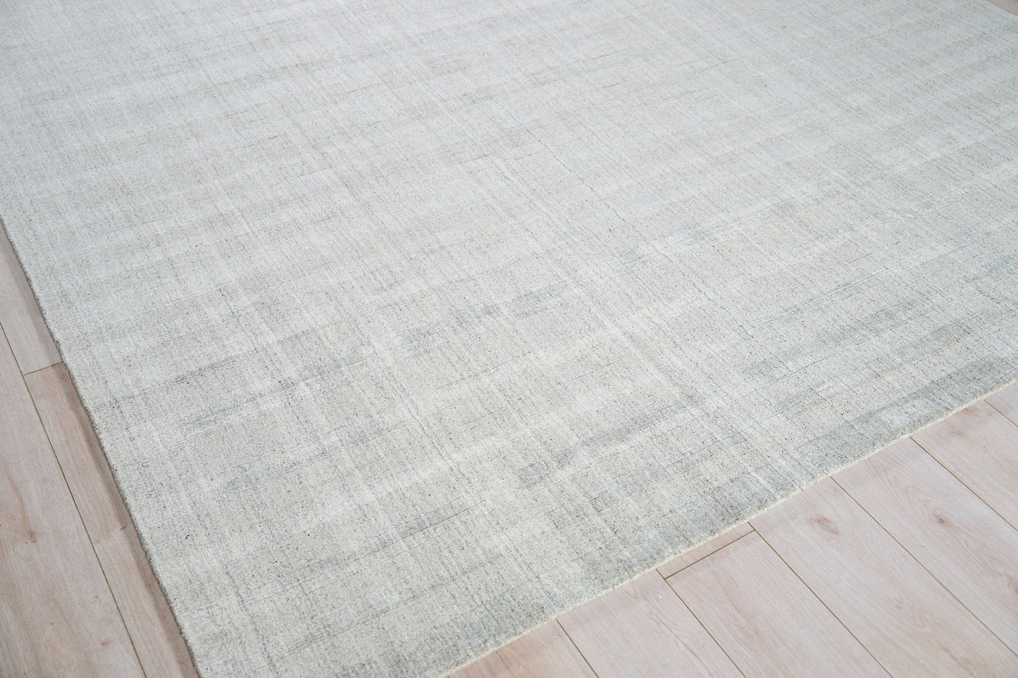 Light gray hand loomed rug with subtle tonal variation on light wood floor; modern minimalist area rug