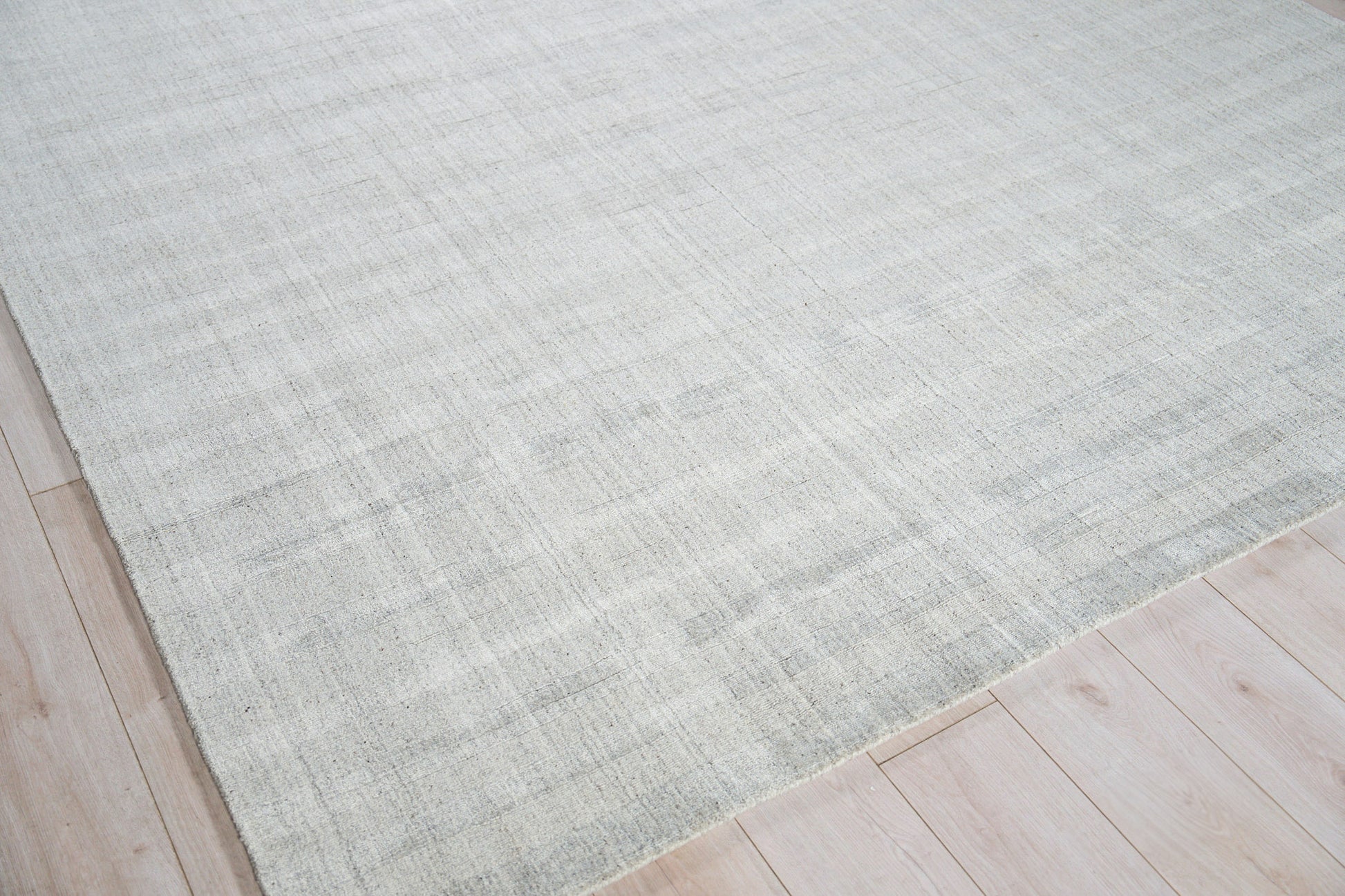 Light gray hand loomed rug with subtle tonal variation on light wood floor; modern minimalist area rug