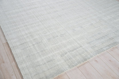 Light gray hand loomed rug with subtle tonal variation on light wood floor; modern minimalist area rug