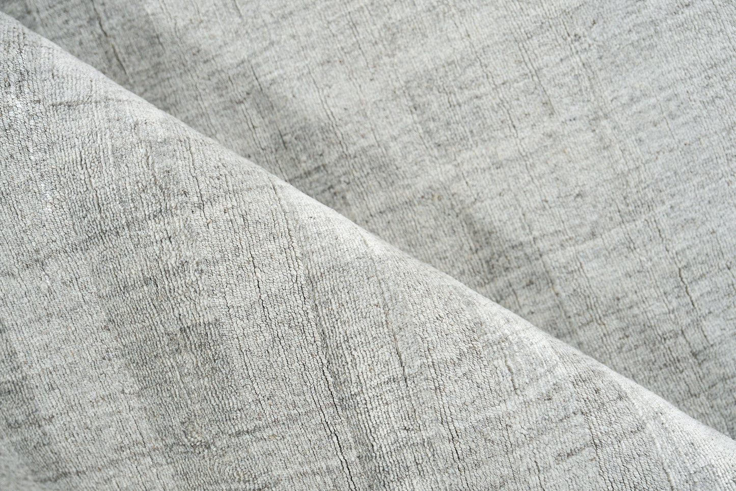 Close-up of a light gray hand-loomed rug with a subtle woven texture and a diagonal fold.