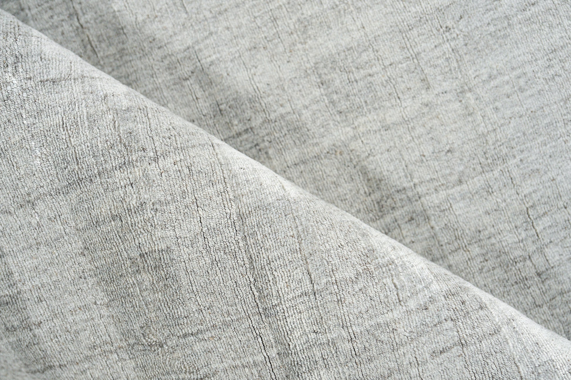 Close-up of a light gray hand-loomed rug with a subtle woven texture and a diagonal fold.