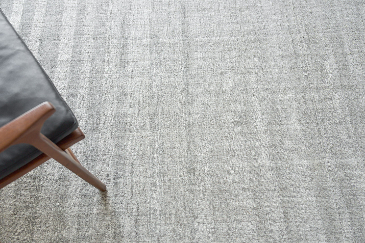 Light gray textured rug with a brown wooden mid-century chair leg and dark gray upholstery.
