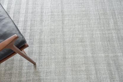 Light gray textured rug with a brown wooden mid-century chair leg and dark gray upholstery.