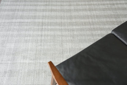 Corner of a striped indoor hand-loomed rug on a gray surface.