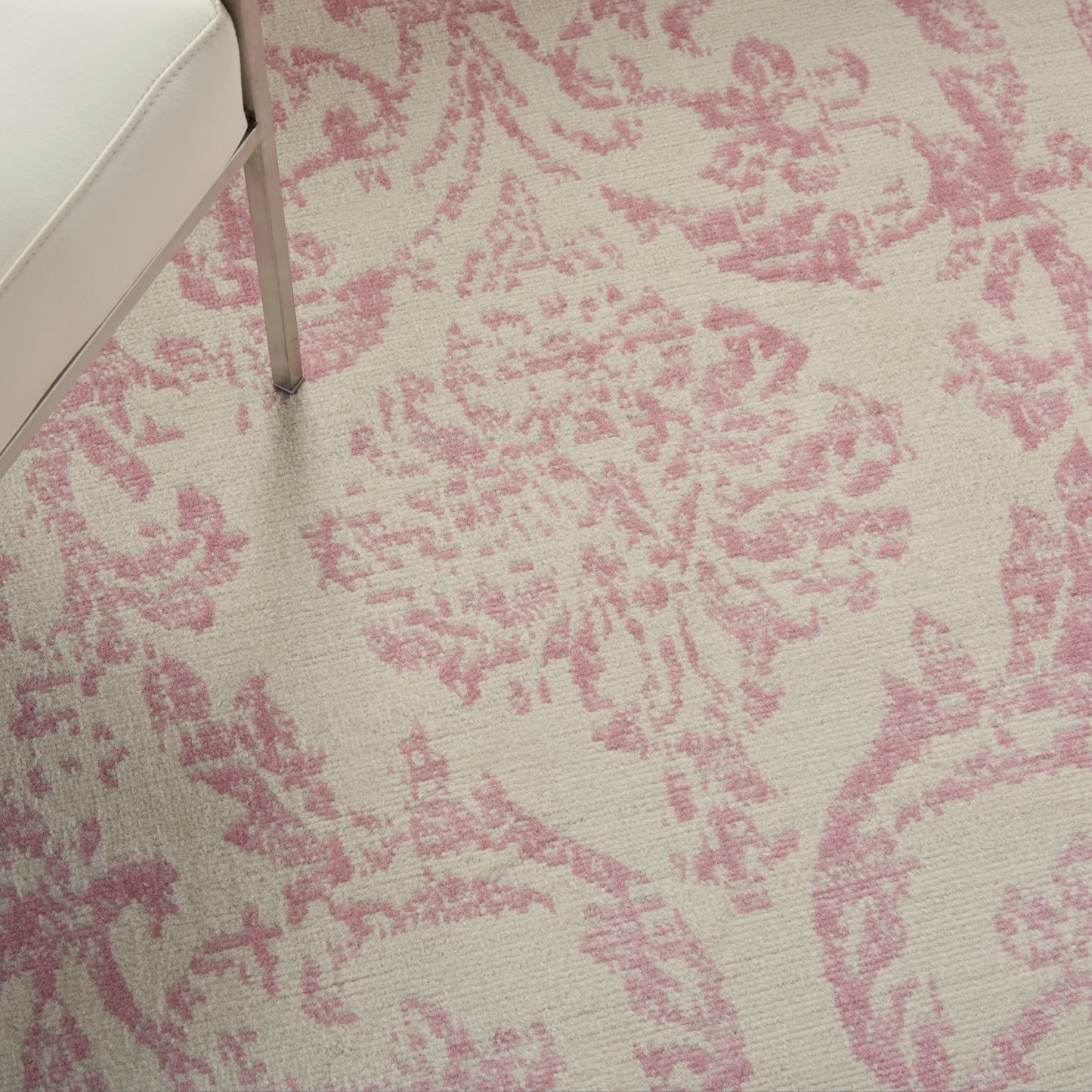 Cream rug with pink damask floral pattern; partial view of a light upholstered chair leg.