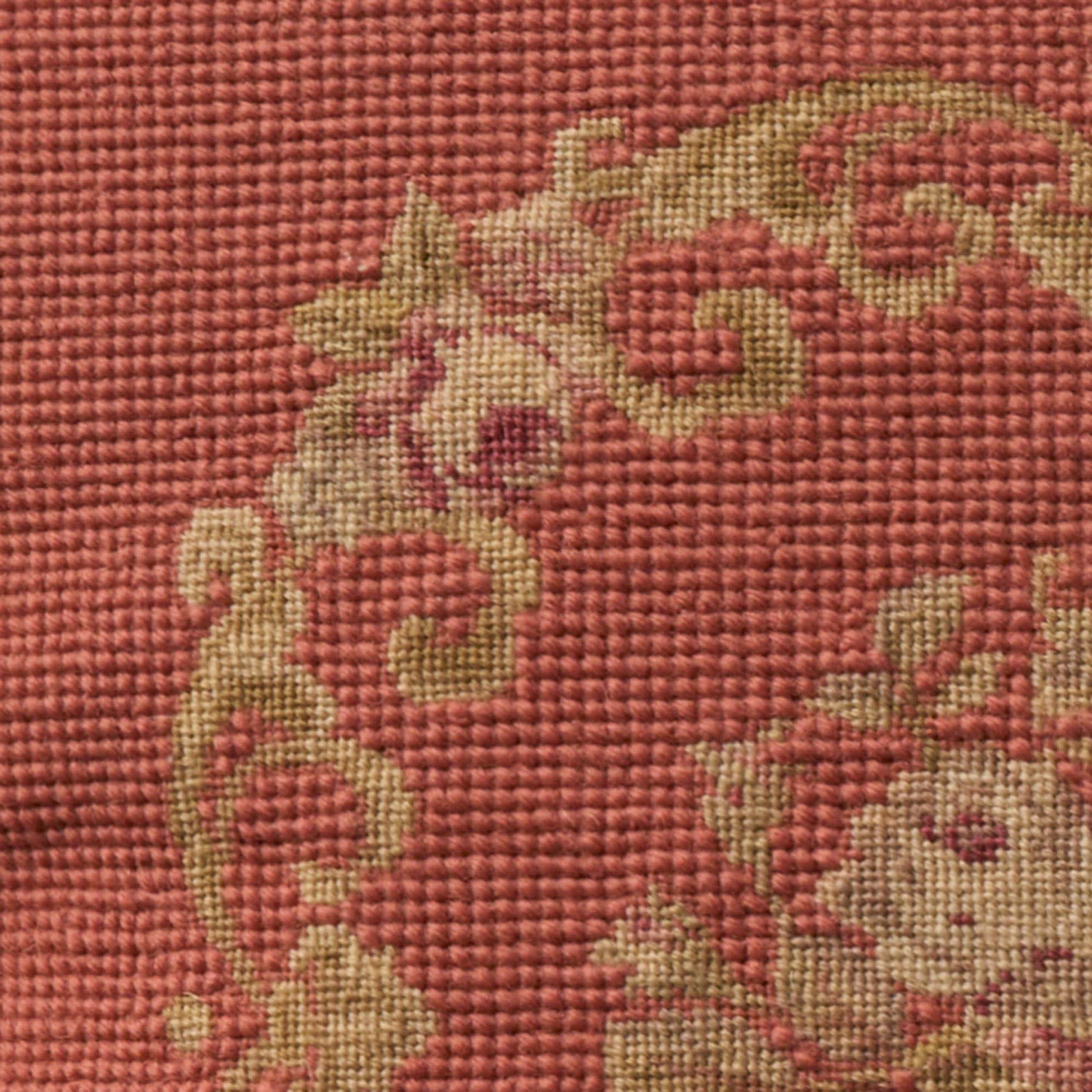 Close-up of red woven fabric with beige-gold baroque floral scroll pattern.
