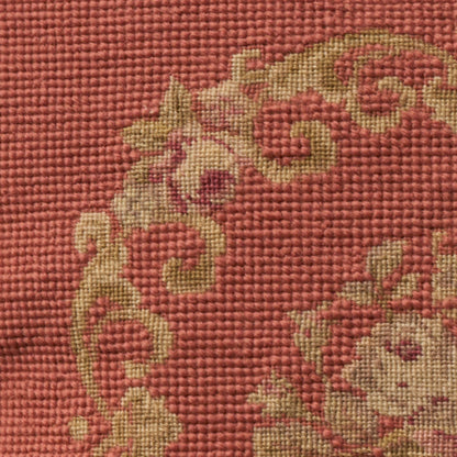 Close-up of red woven fabric with beige-gold baroque floral scroll pattern.