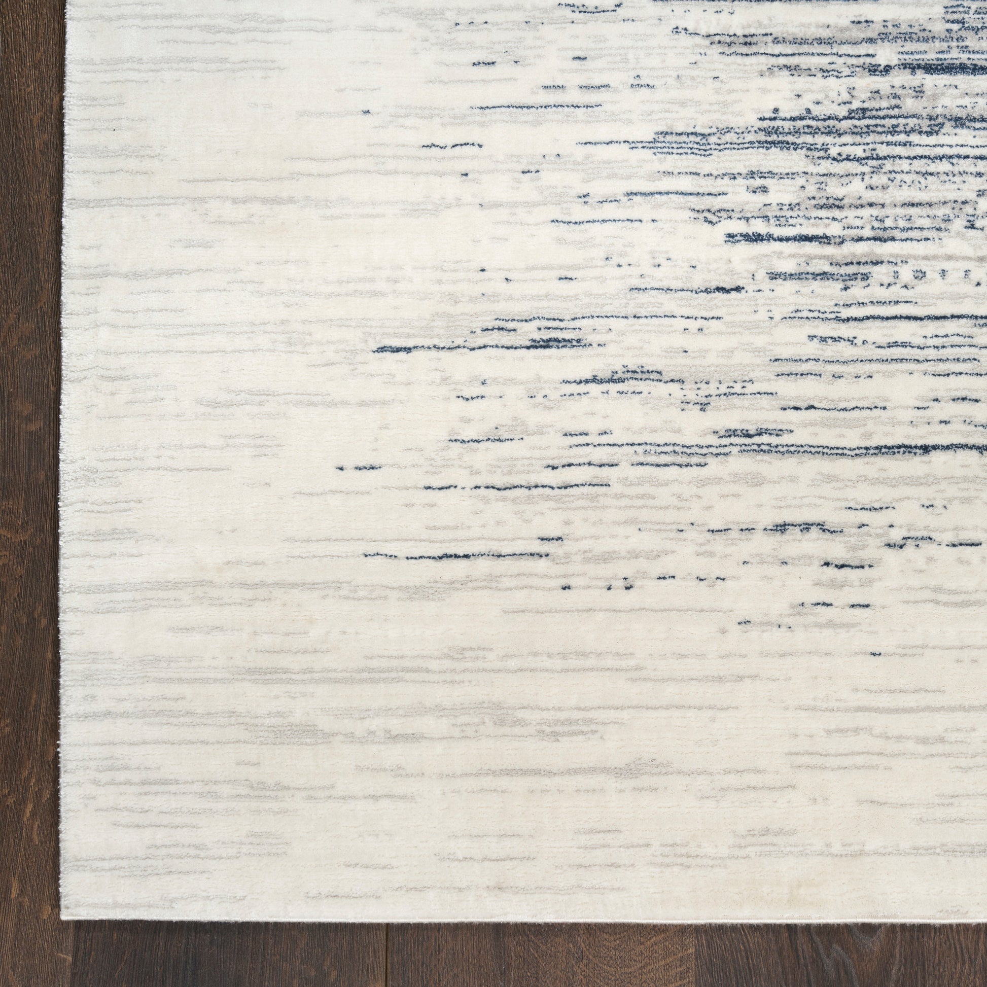 Cream flat-weave rug with blue distressed brush-stroke lines on dark wood floor.