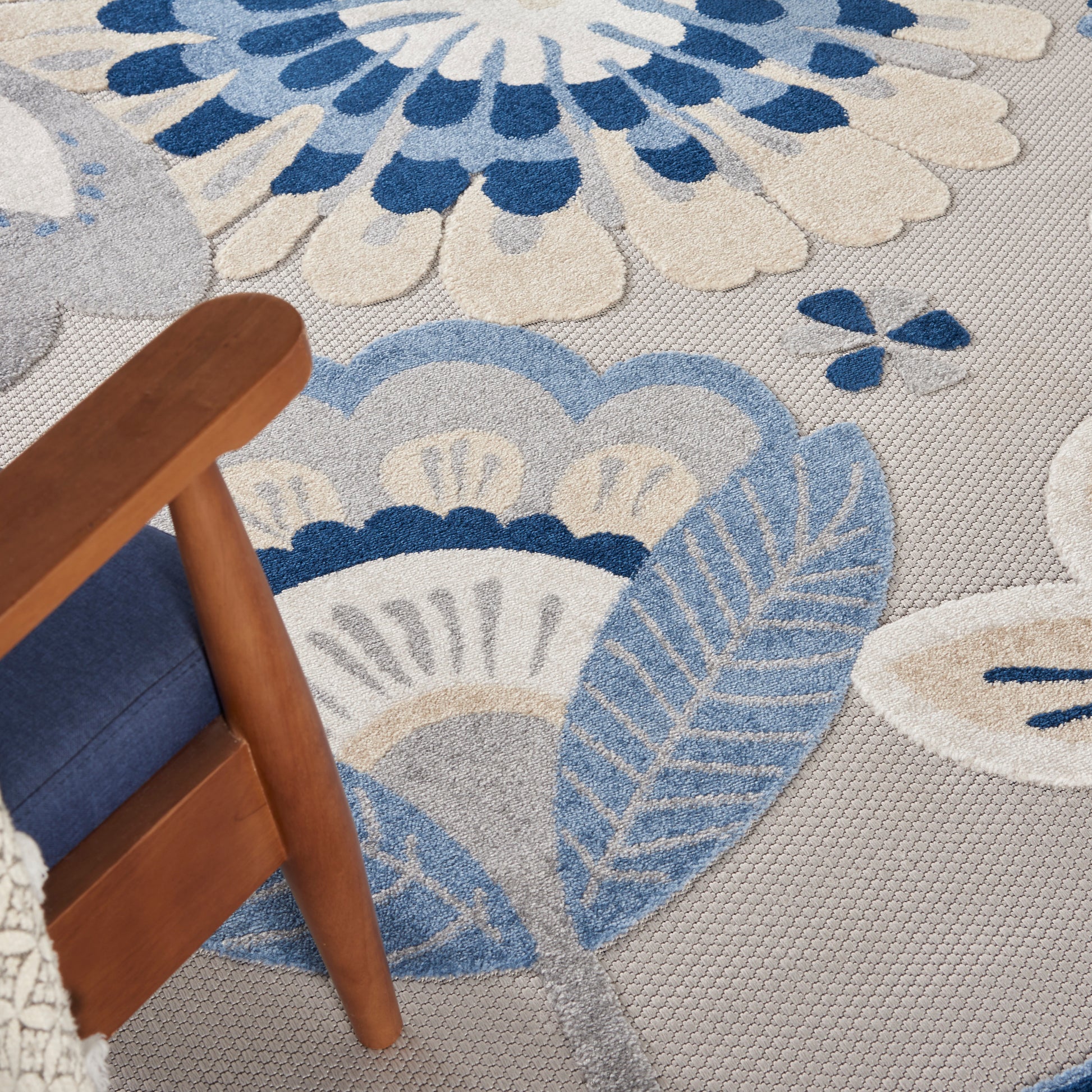 Soft gray-blue patterned area rug with floral/leaf motifs in blue hues; wooden chair with blue cushion.