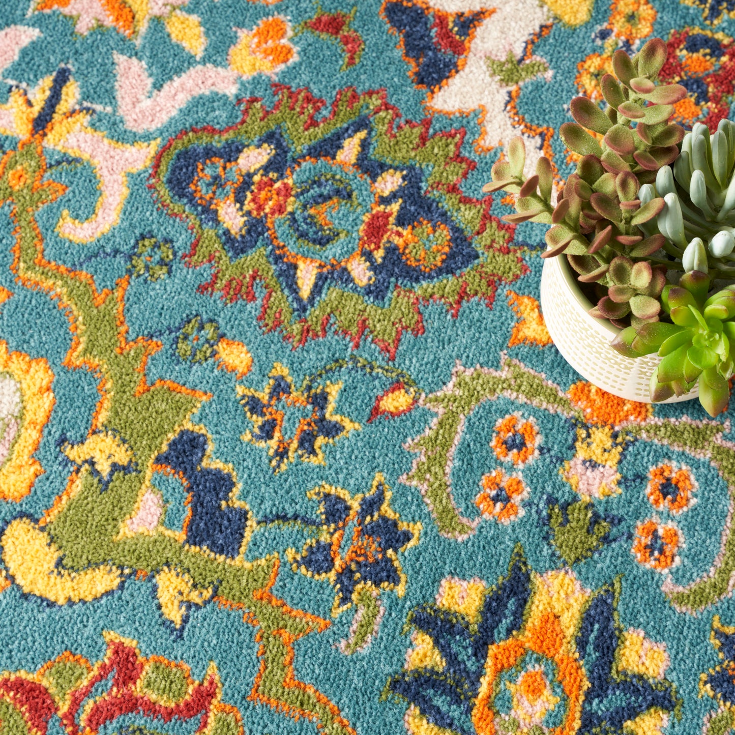 Vibrant teal rug with multicolor oriental pattern in orange, yellow, green, blue; succulent plant in beige pot on the right